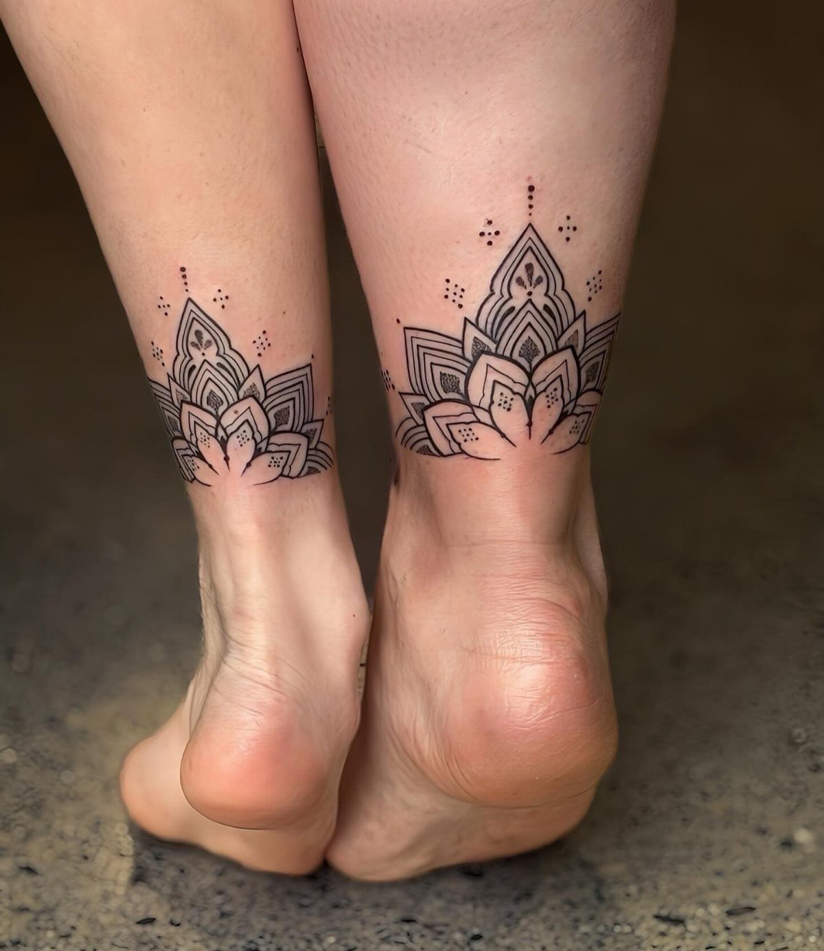 Matching black ink lotus flower tattoos on two people's ankles and heels.