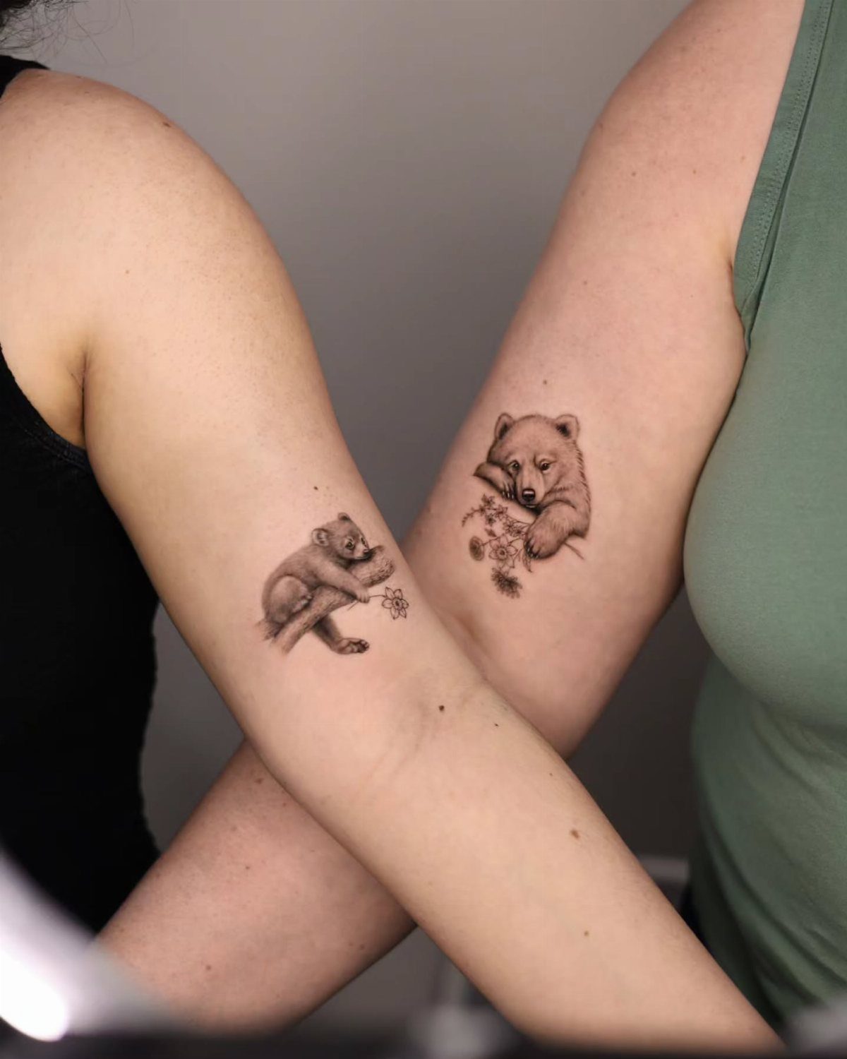 Two arms crossed showing matching bear cub tattoos in black and grey ink.