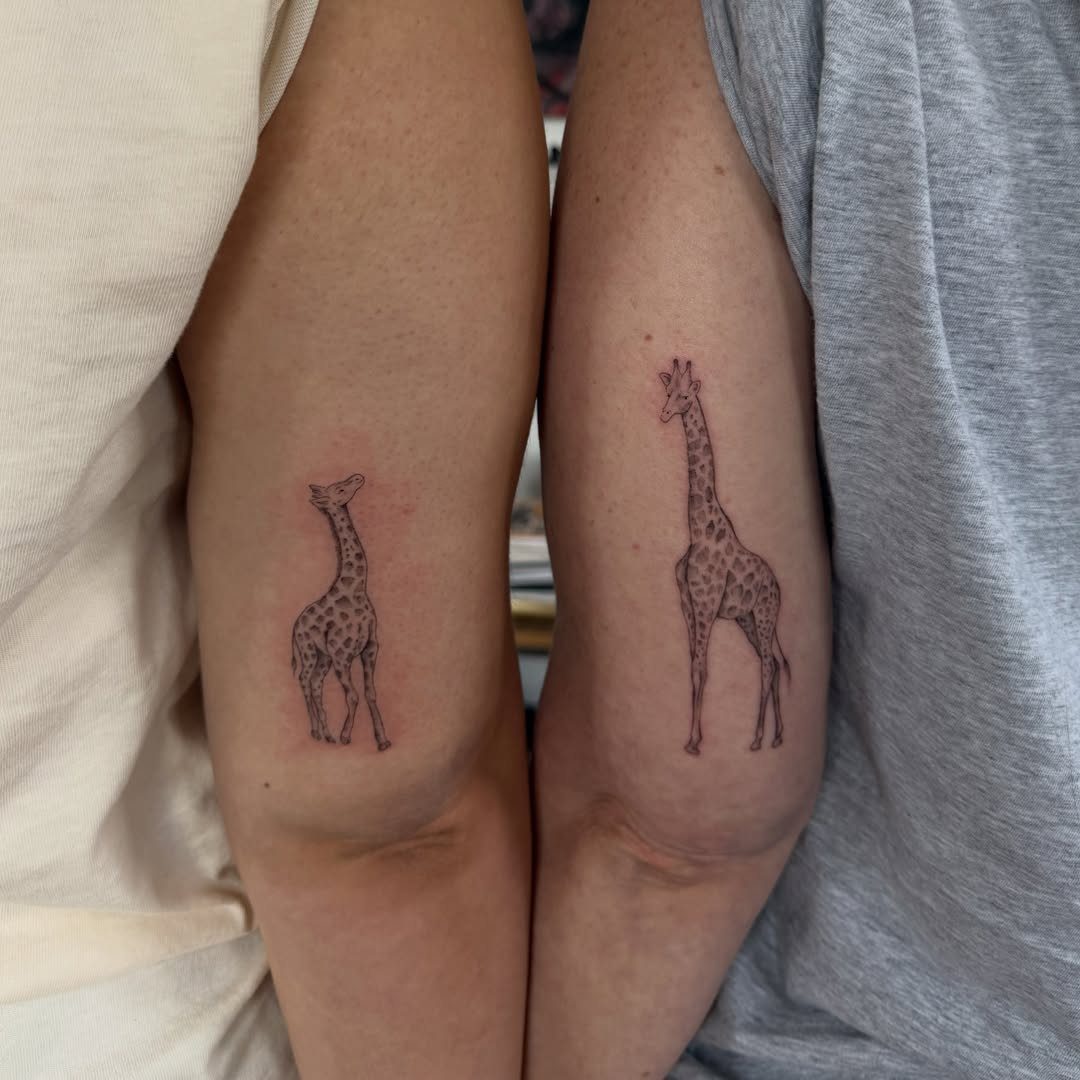 Two matching giraffe tattoos on the upper arms of two different people.