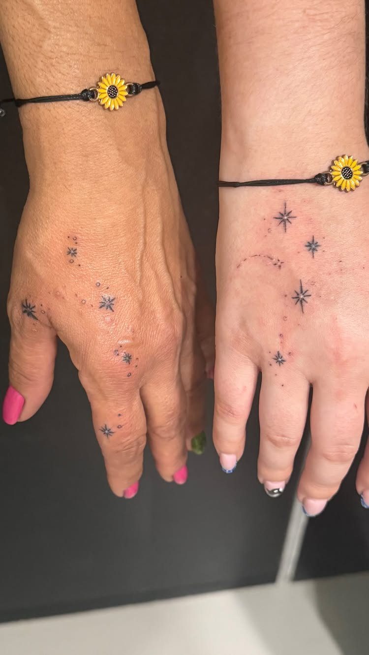 Two hands with matching small black star tattoos and sunflower wrist bracelets.
