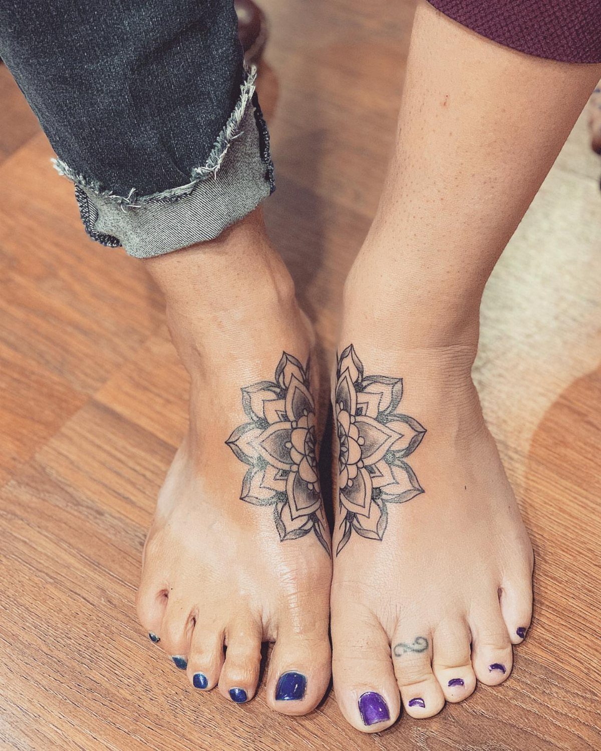 Matching black ink mandala tattoos on the tops of two people's feet.