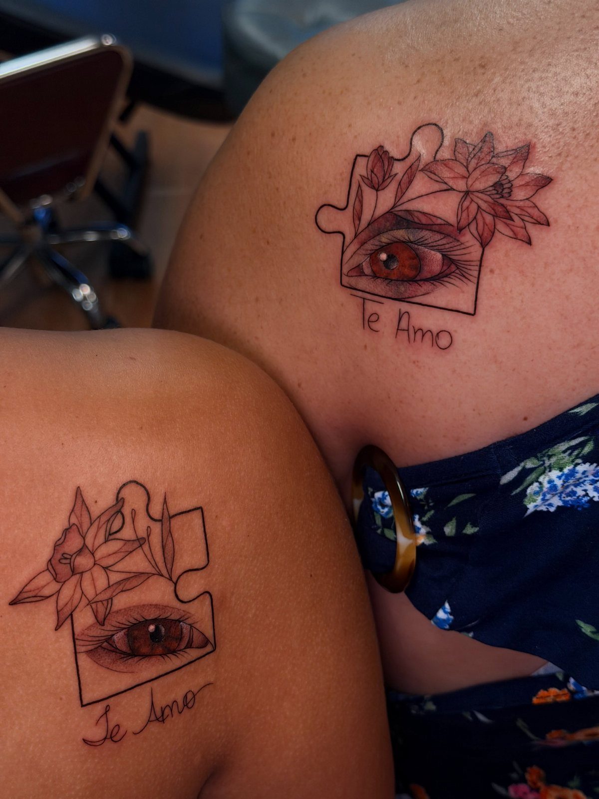 Matching puzzle piece tattoos on two shoulders featuring eyes, flowers, and Te Amo text.