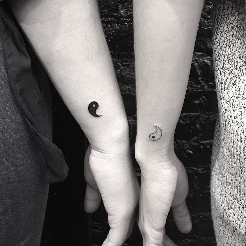Two inner wrists with matching half yin yang tattoos forming a complete symbol.