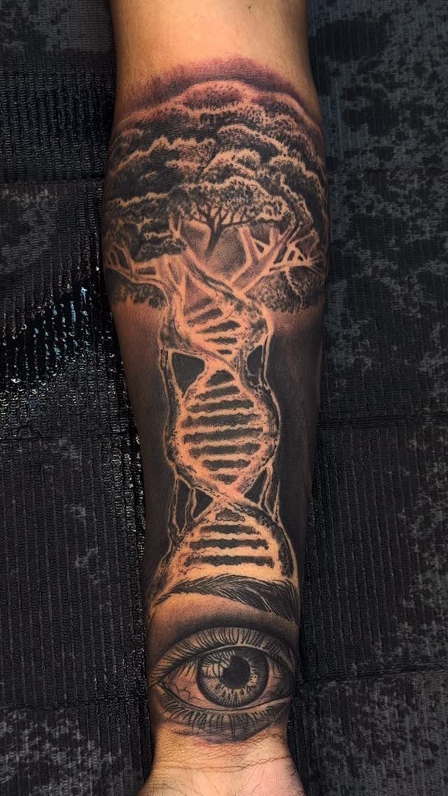 Tattoo on a forearm showing a tree with a DNA helix trunk and eye.