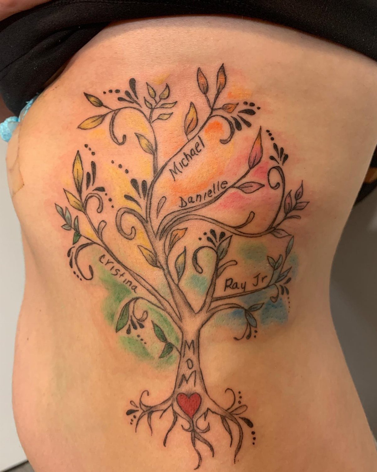 Family tree tattoo on torso with names, watercolor accents, and a red heart root.
