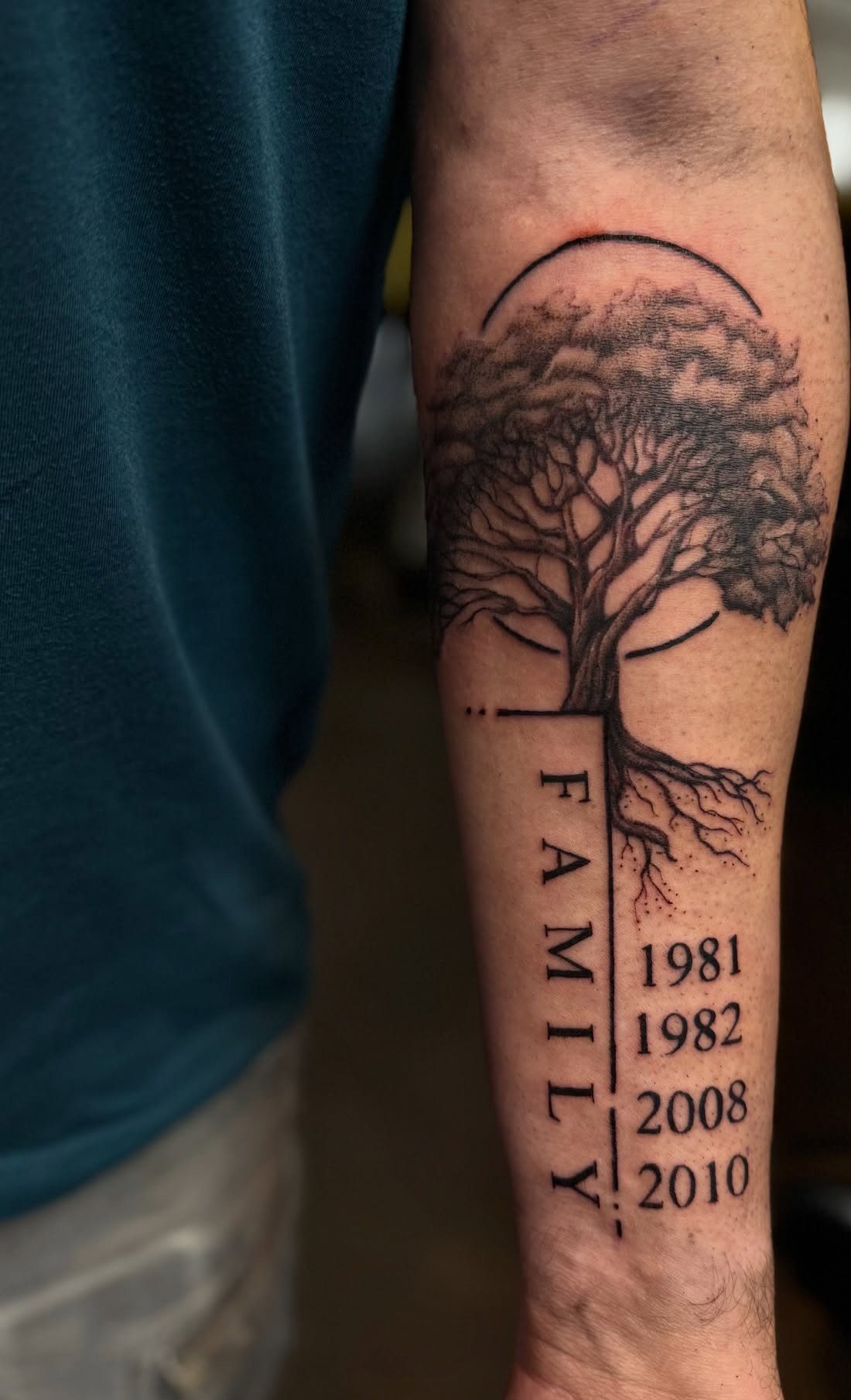 Family tree tattoo on a forearm featuring the word FAMILY and four birth years.