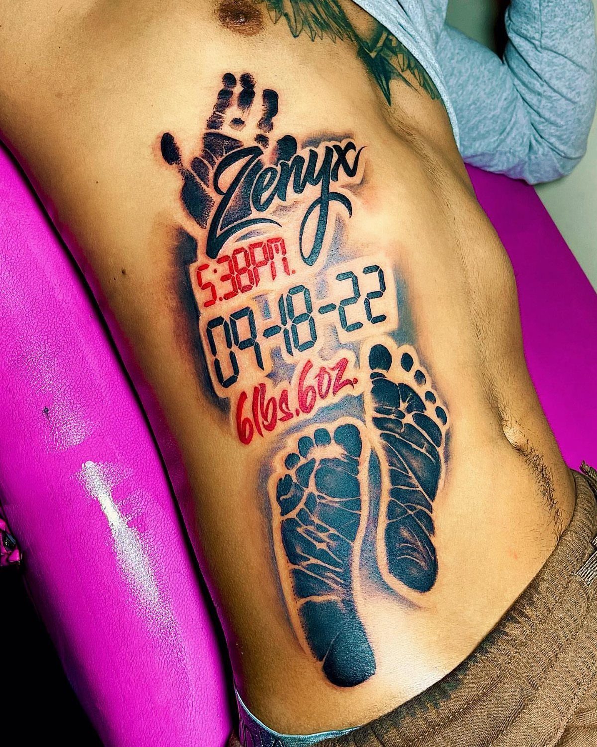 Tattoo on a torso showing baby footprints, handprint, name, date, and birth weight.
