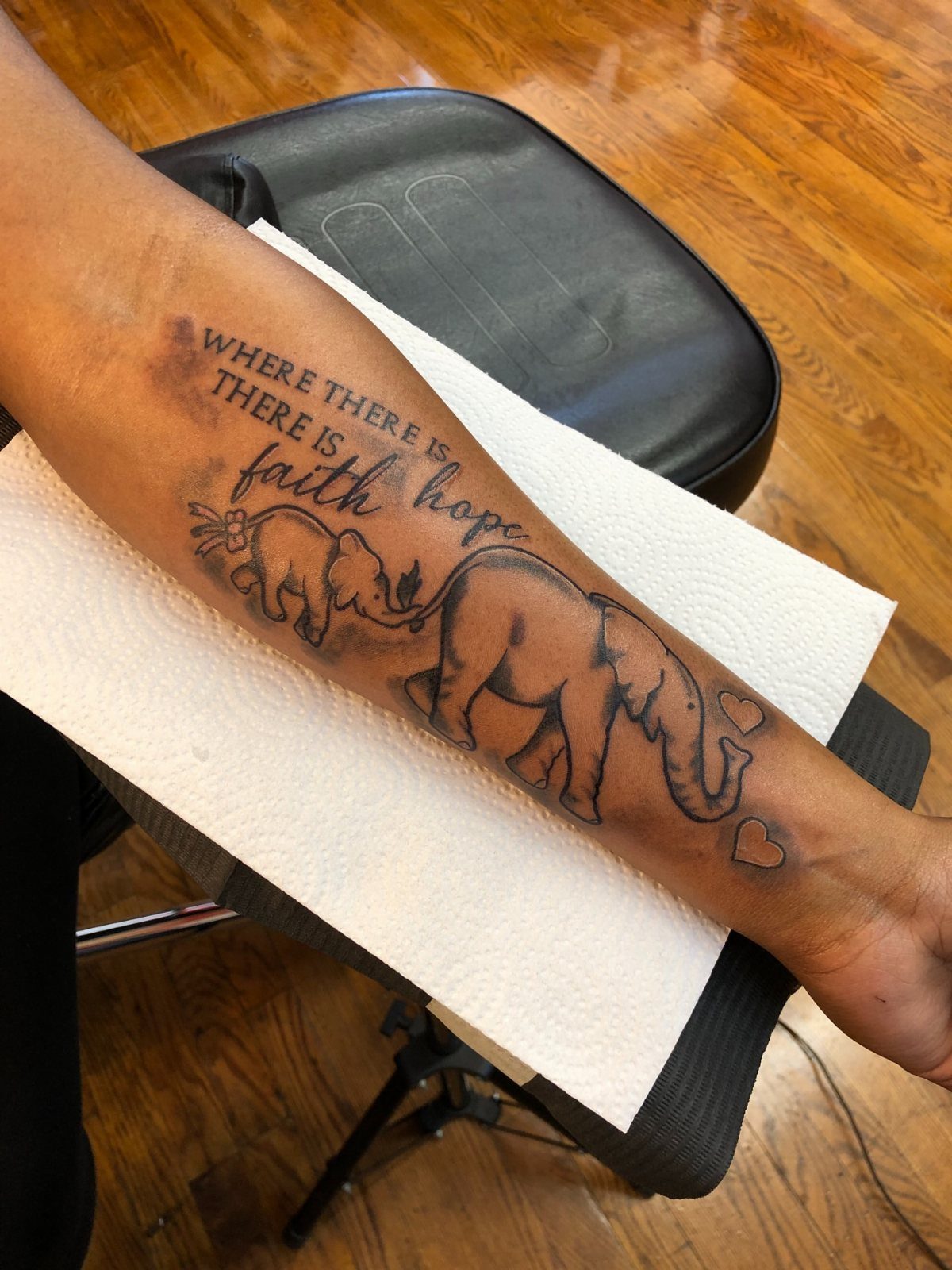 Elephant tattoo on forearm showing a parent and baby elephant with inspirational text.