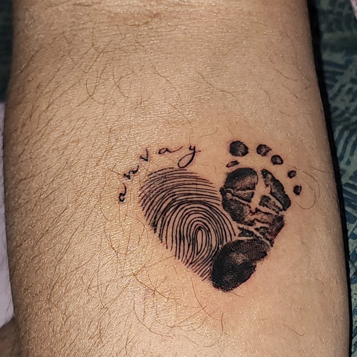 Heart tattoo combining a fingerprint and baby footprint with a name on skin.