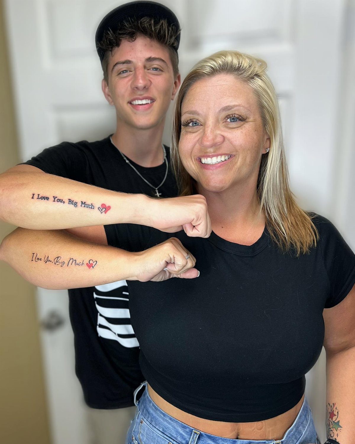 Mother and son posing to show matching forearm tattoos with text and hearts.