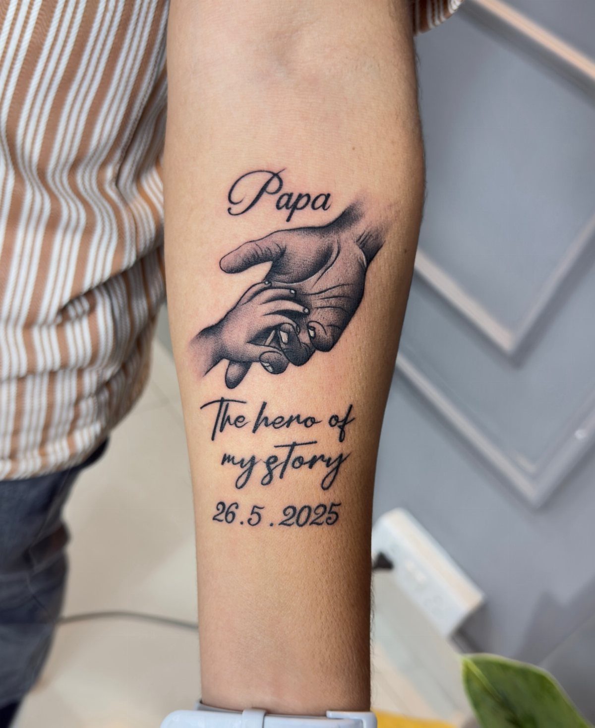 Tattoo on forearm showing a father and child holding hands with text.