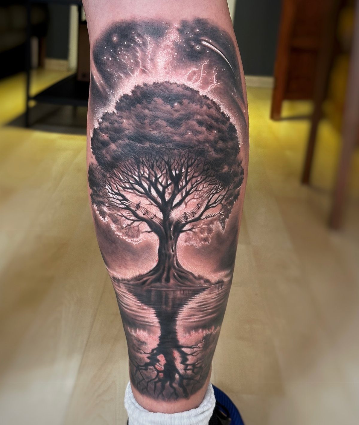 Tree of life tattoo with cosmic background and water reflection on a leg.
