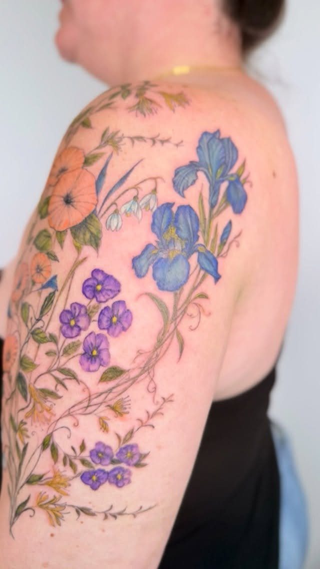 Colorful floral tattoo on a shoulder featuring blue irises and orange poppies.