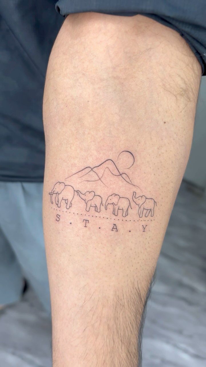 Line tattoo of a family of elephants walking under mountains on a calf