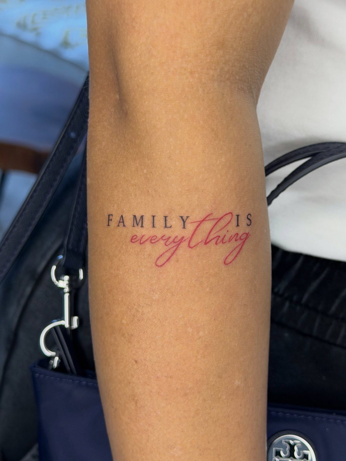 Forearm tattoo with the words FAMILY IS everything in black and red ink