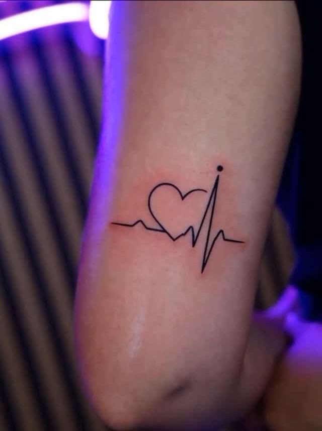 Heartbeat EKG line tattoo with a heart shape on a person's arm