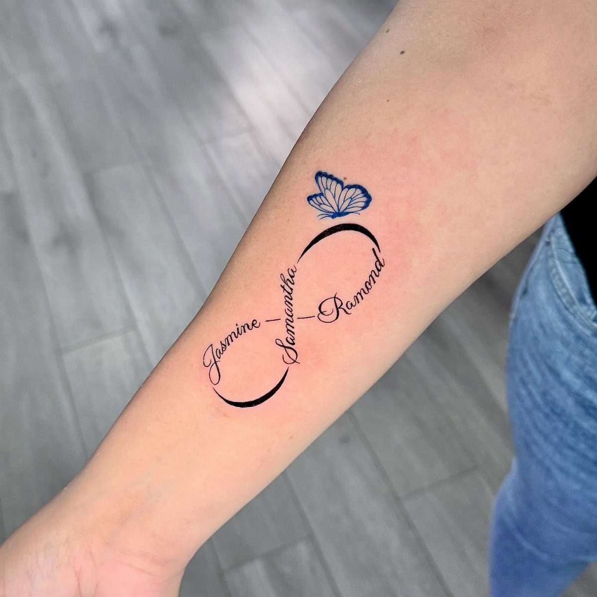 Infinity symbol tattoo with names Jasmine, Samantha, and Raymond and a blue butterfly