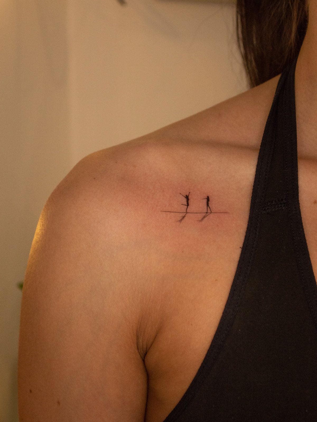 Minimalist silhouette tattoo of a mother and child on a person's shoulder