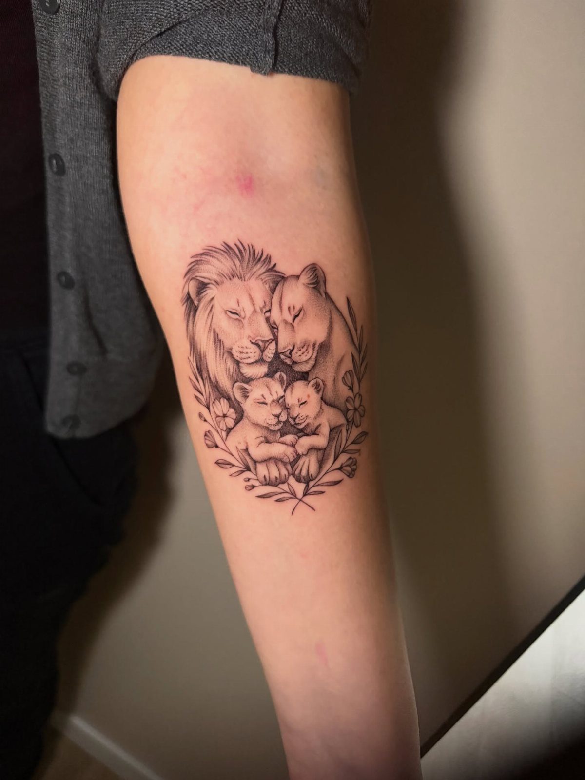 Lion family tattoo with two adults and two cubs surrounded by floral accents