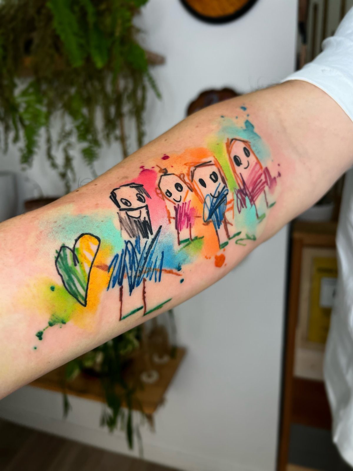 Watercolor tattoo on a forearm showing a family of four and a heart.