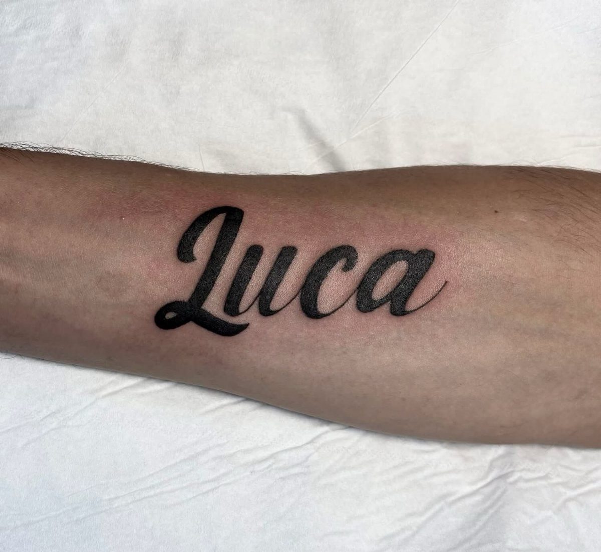 Cursive name tattoo of Luca in black ink on a person's forearm
