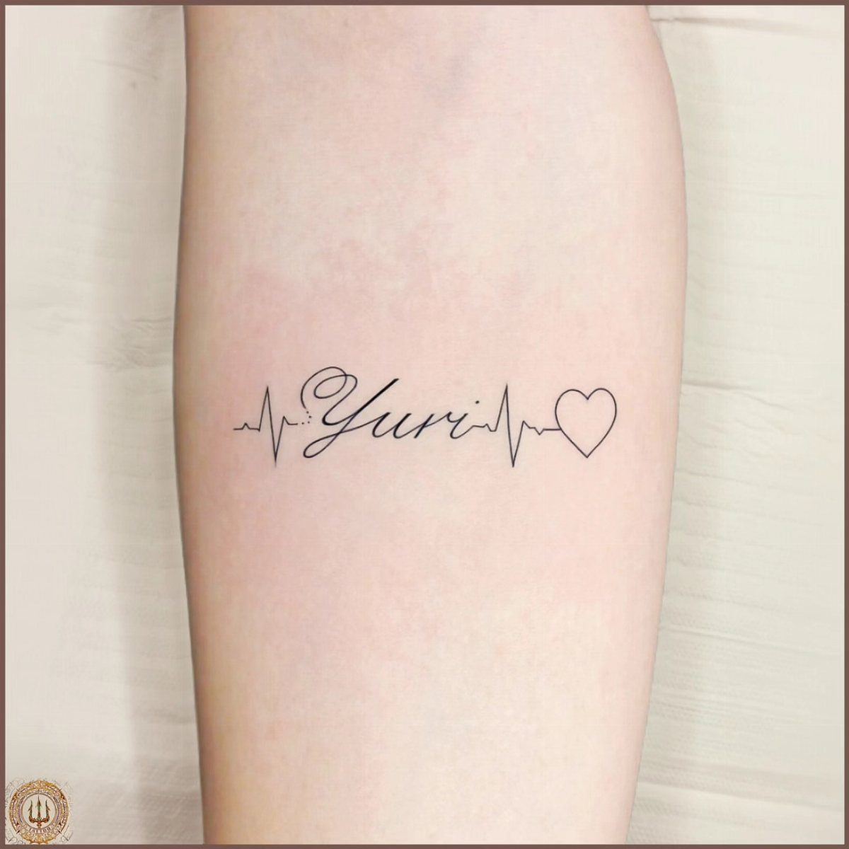 Heartbeat line tattoo transitioning into the cursive name Yuri and a small heart.