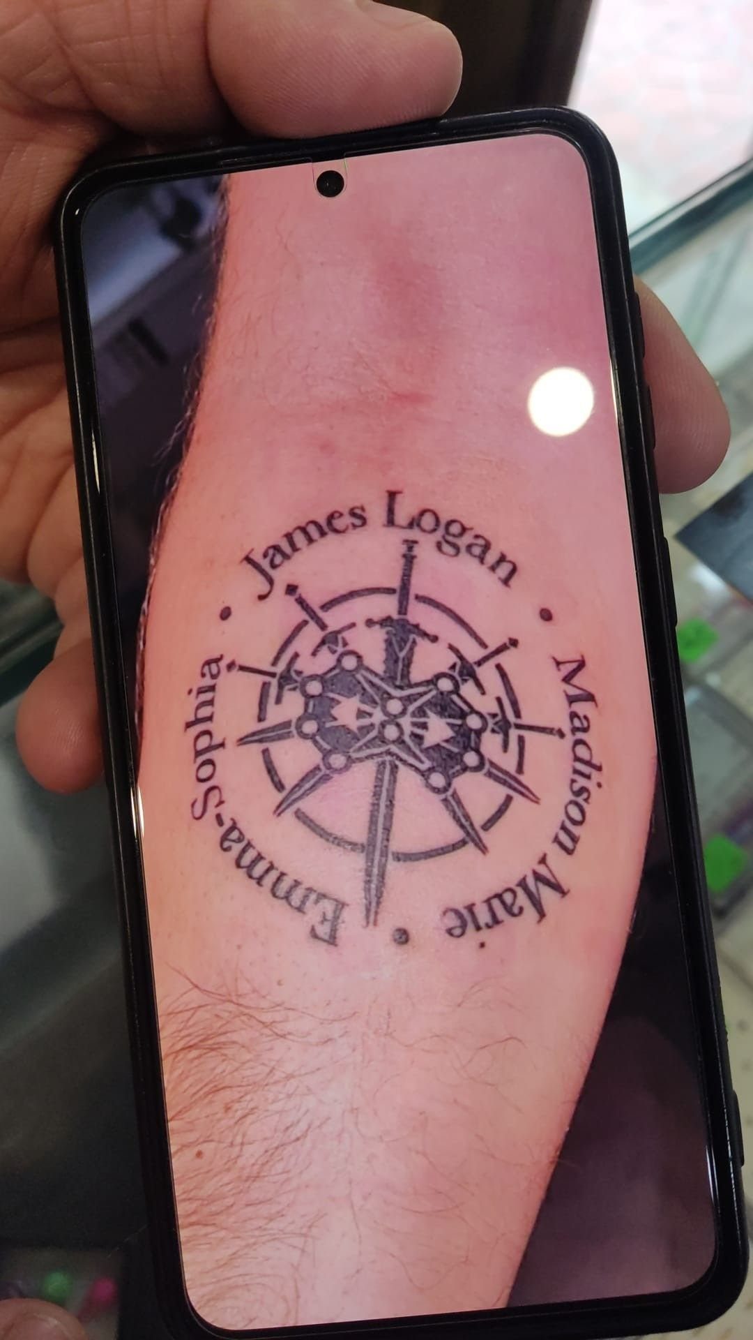 Nautical compass tattoo on a forearm surrounded by three names in black ink.