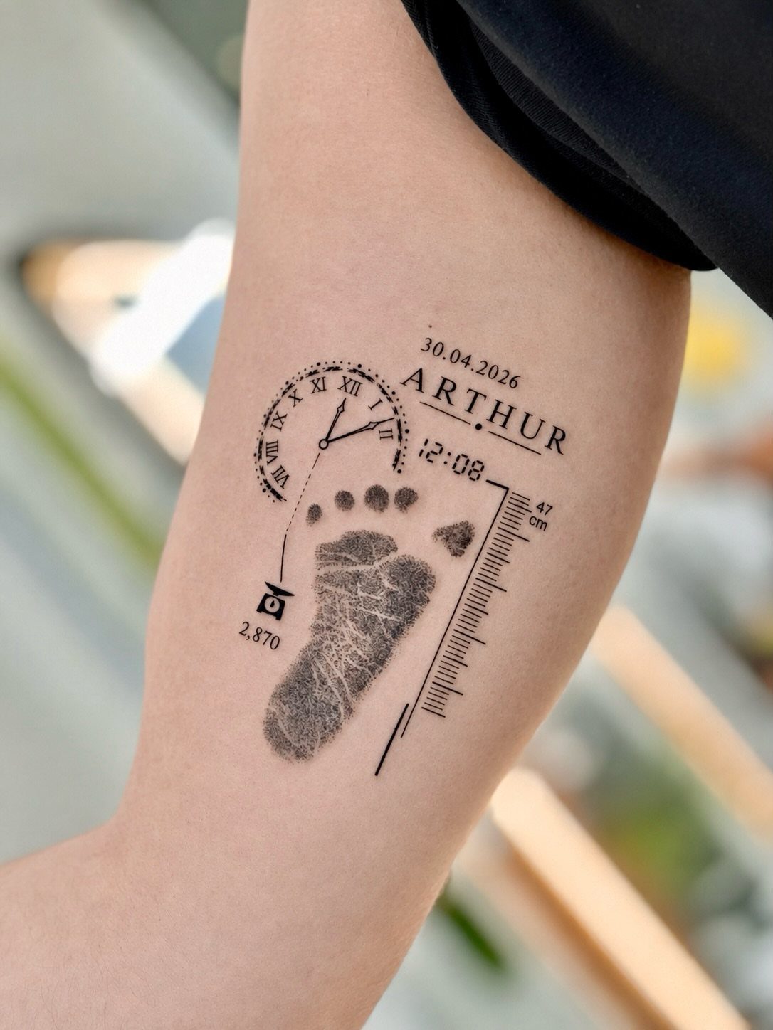 Tattoo on a forearm showing the name Arthur with a baby footprint and clock.