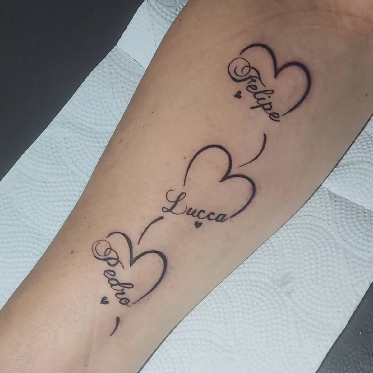 Three forearm tattoos of names Felipe, Lucca, and Pedro integrated with heart shapes.