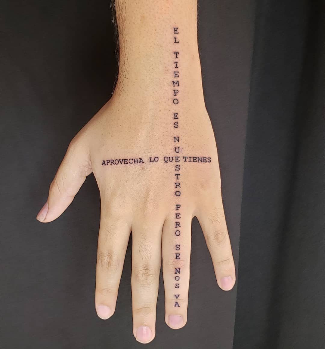 Hand and wrist with black ink Spanish lettering tattoos arranged in a cross