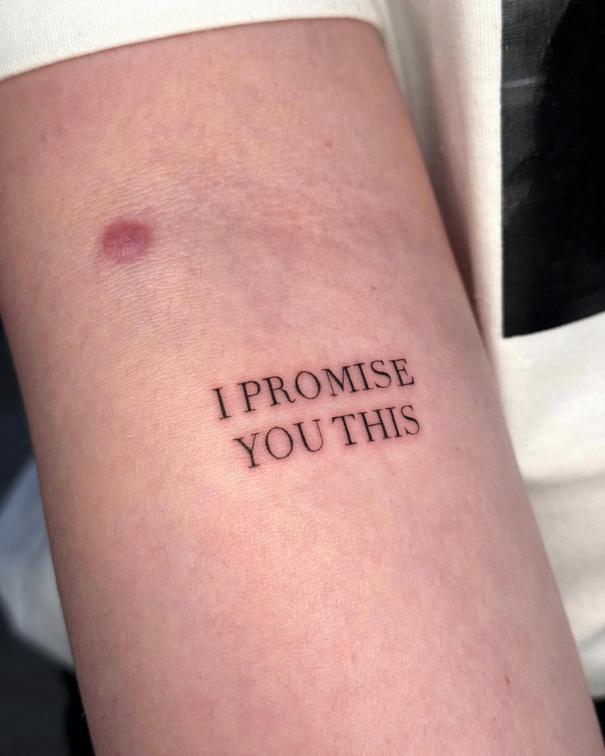 Small black ink tattoo on an arm reading I PROMISE YOU THIS