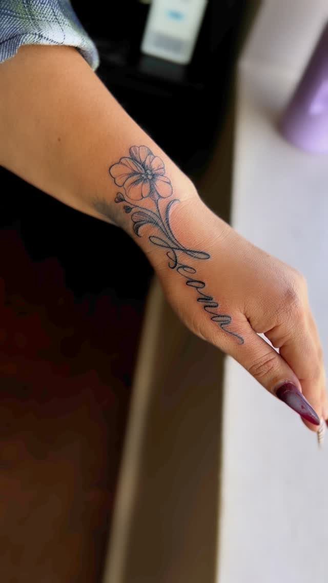 Cursive name tattoo with a flower on a person's forearm and hand