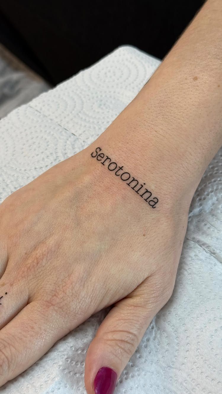 Small black serif tattoo reading Serotonina on a person's inner wrist