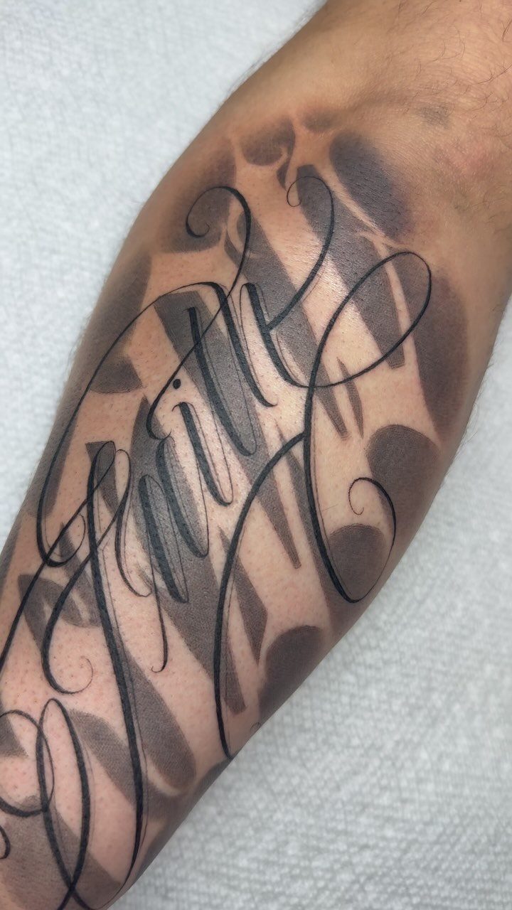 Cursive script tattoo with flowing black ink lettering on a person's forearm