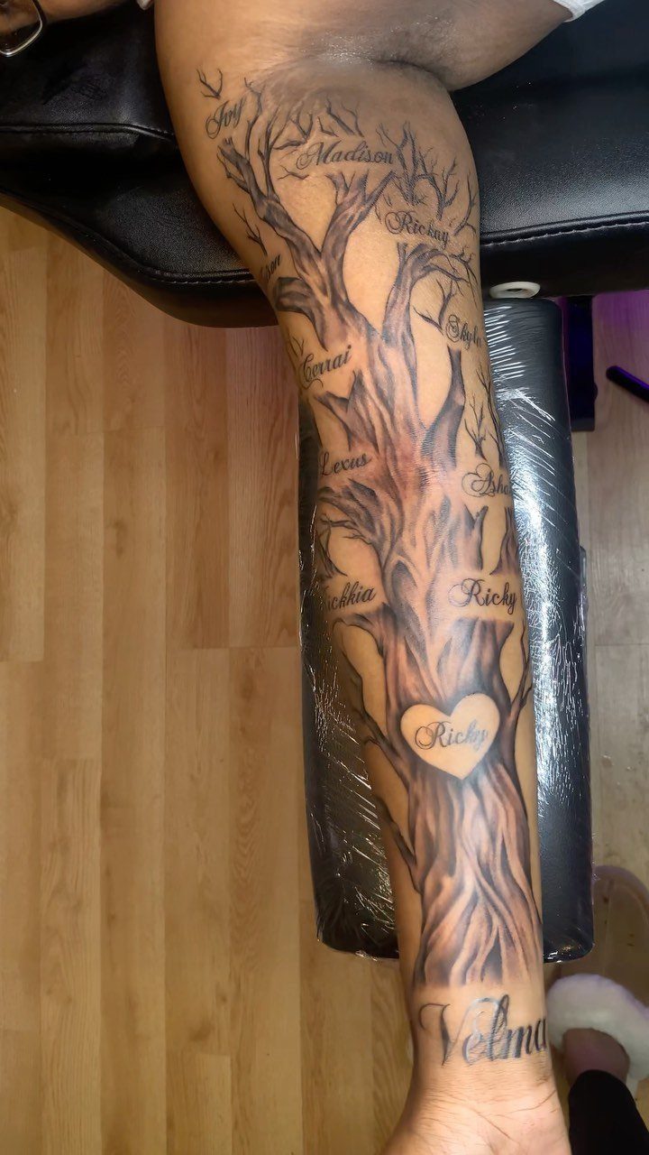 Family tree tattoo on a leg with names integrated into the branches and trunk