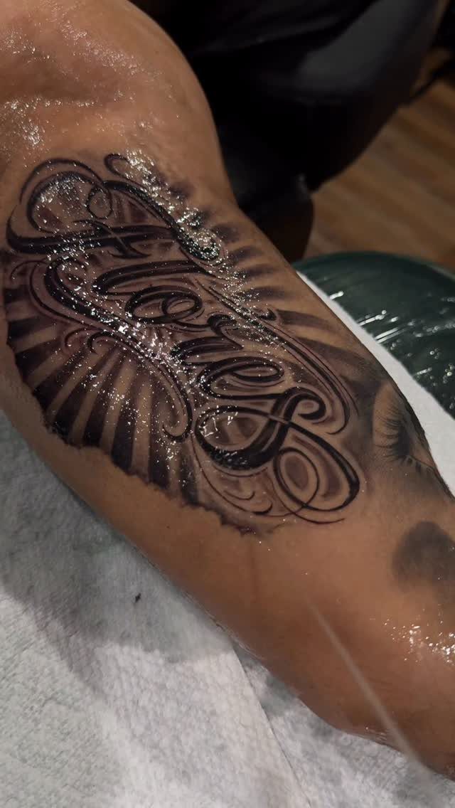 Ornate cursive tattoo of the name Flores on a person's arm with shading.