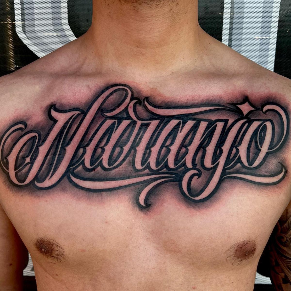 Large cursive Naranjo name tattoo across a man's upper chest with shading.