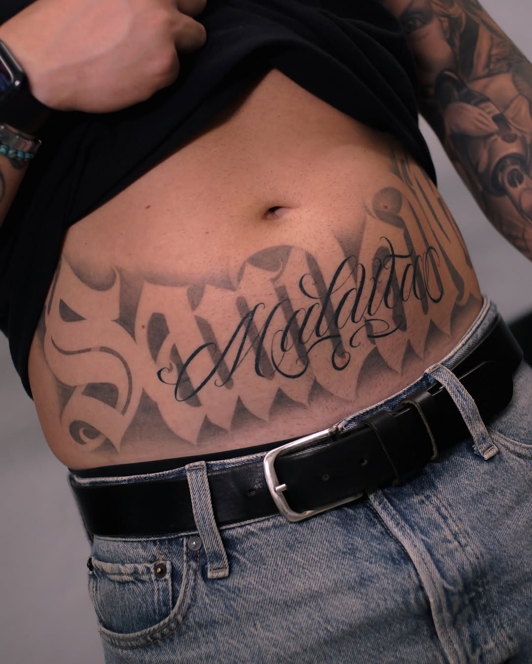 Large black ink script tattoo on a person's stomach above blue jeans.