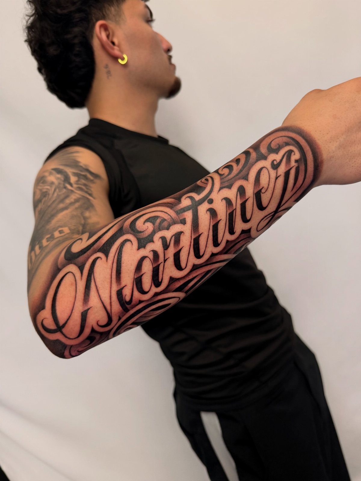 Ornate Martinez last name tattoo in black ink on a man's forearm.