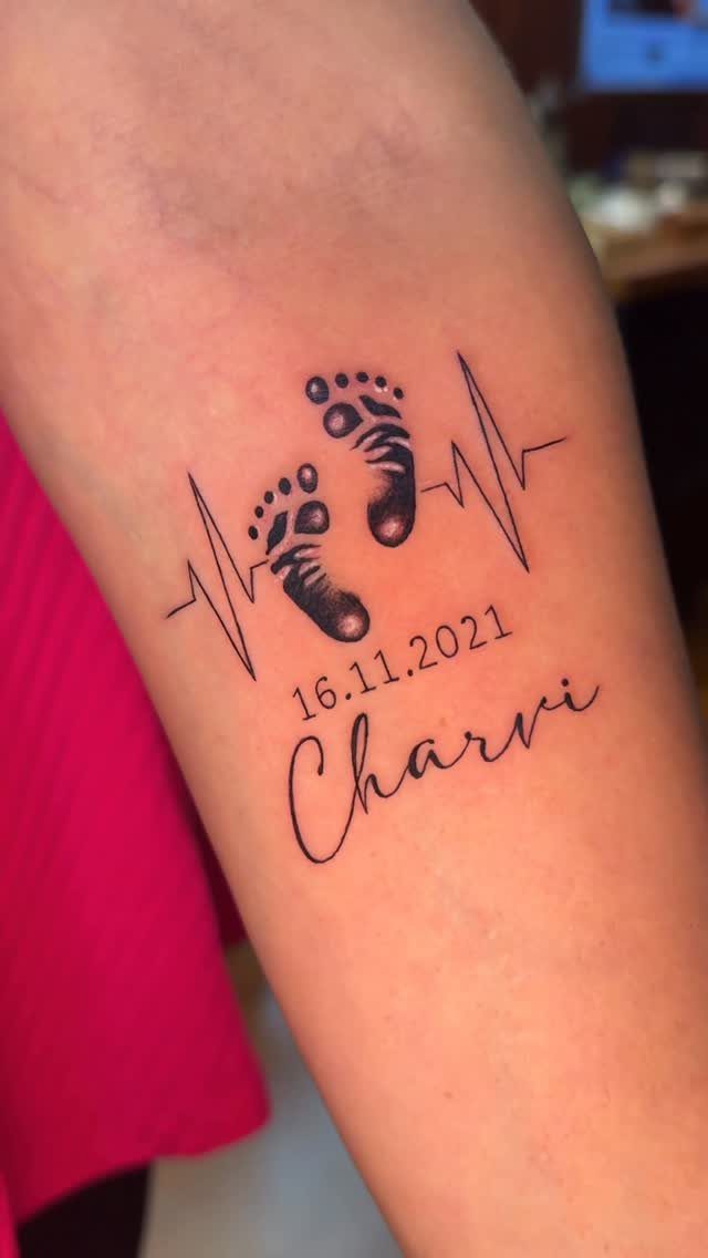 Tattoo on a forearm featuring baby footprints, a heartbeat line, date, and name Charvi.