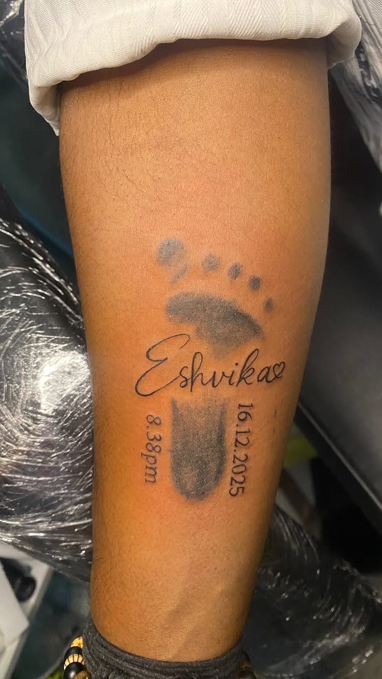 Baby footprint tattoo with the name Eshvika and a date on a forearm.