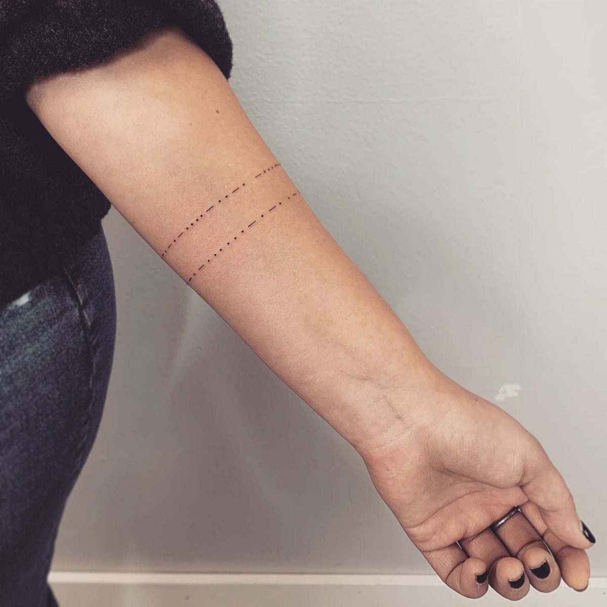 Forearm with two parallel lines of Morse code tattoos in black ink.