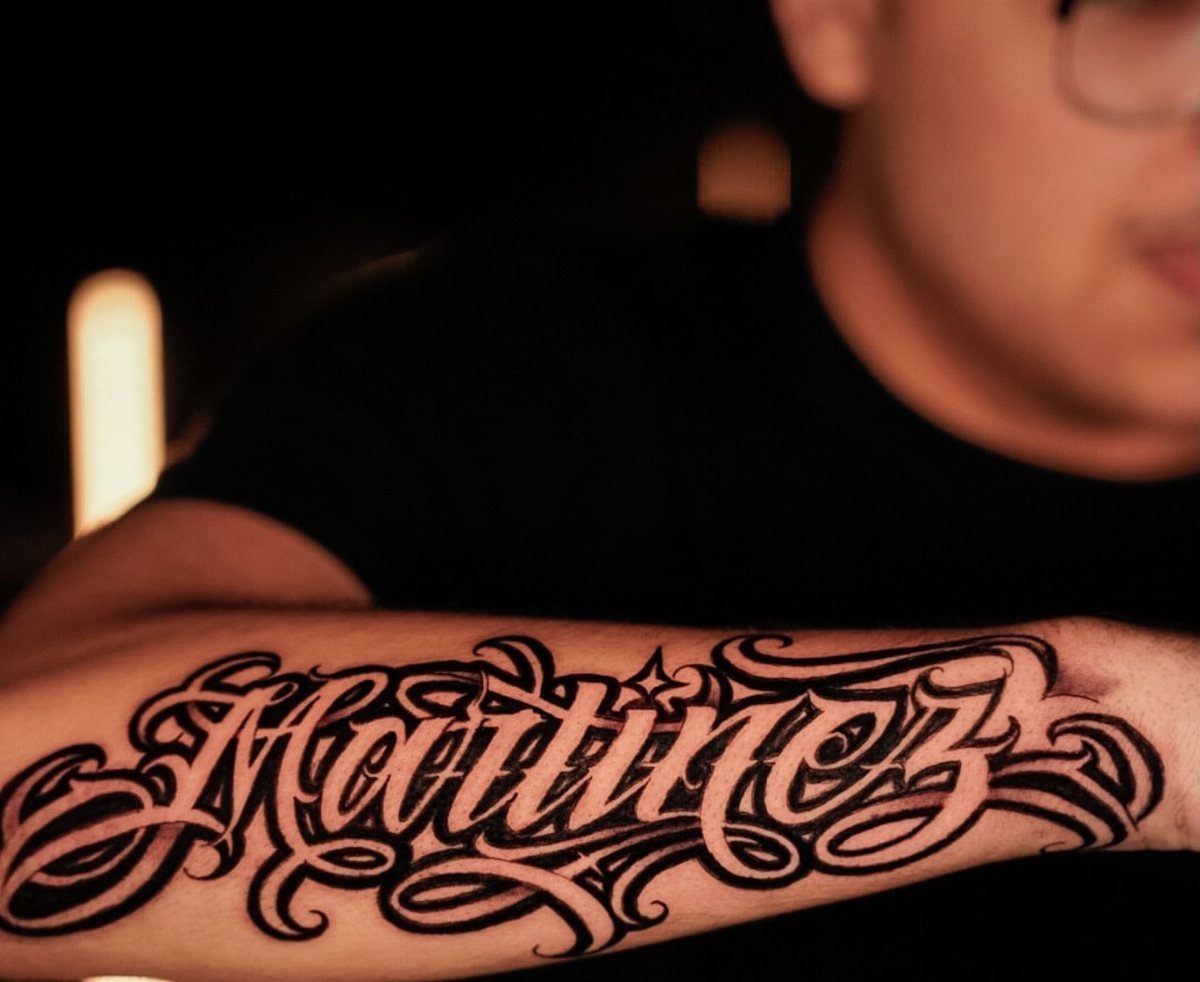 Ornate black ink tattoo of the name Martinez on a person's forearm