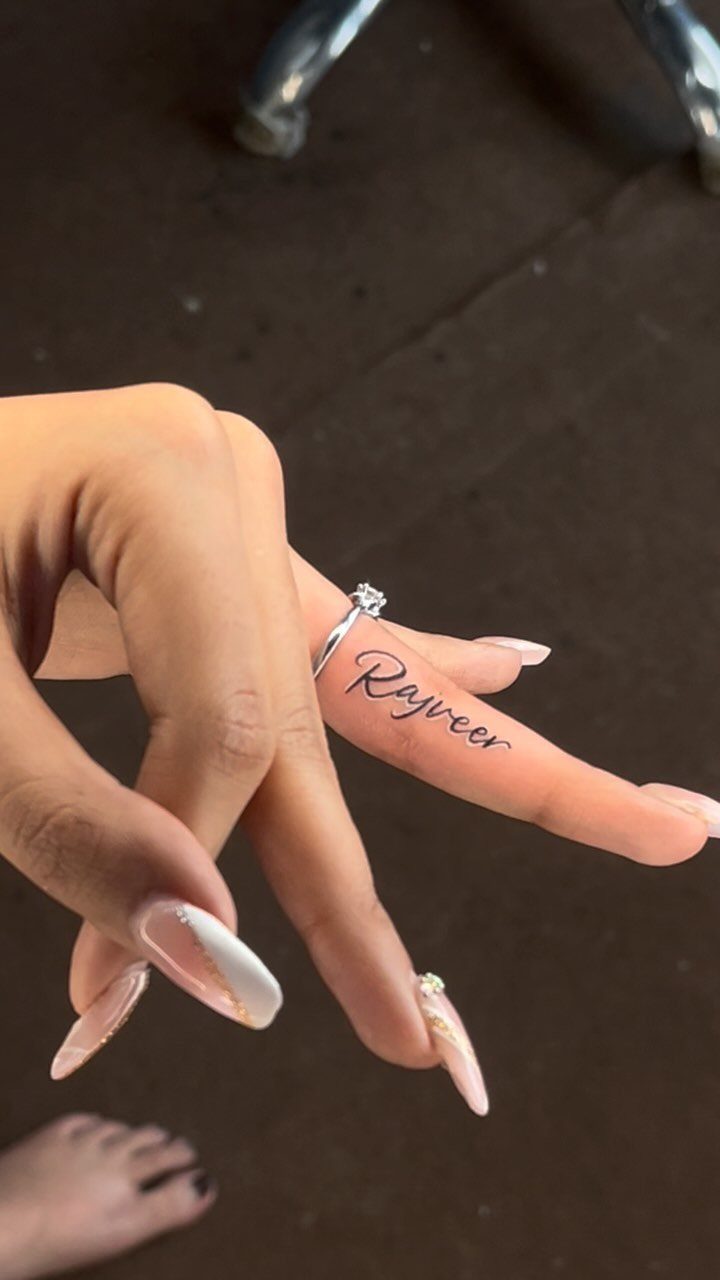 Cursive name tattoo on the side of a ring finger with a diamond ring