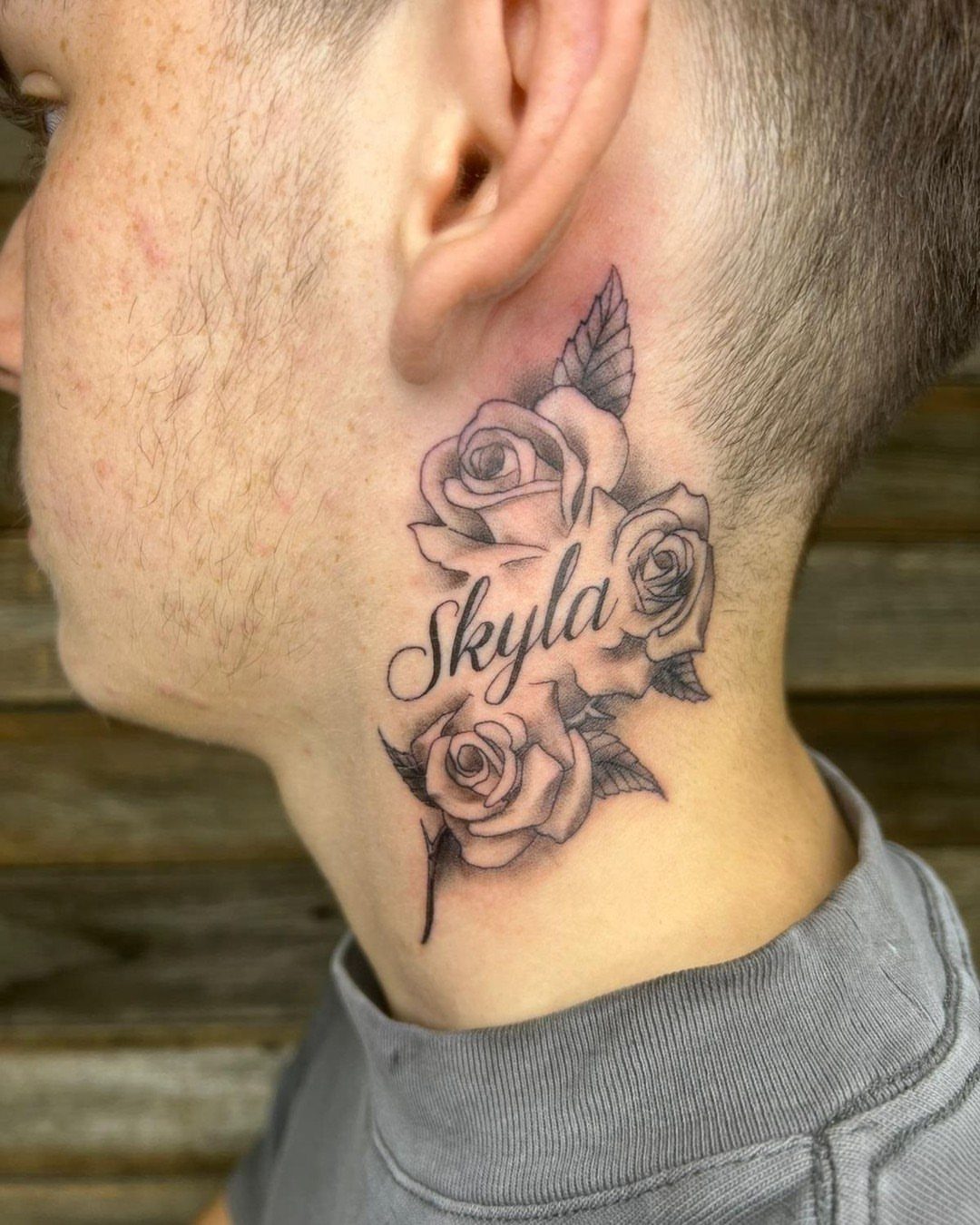 Neck tattoo of the name Skyla surrounded by detailed black and grey roses.