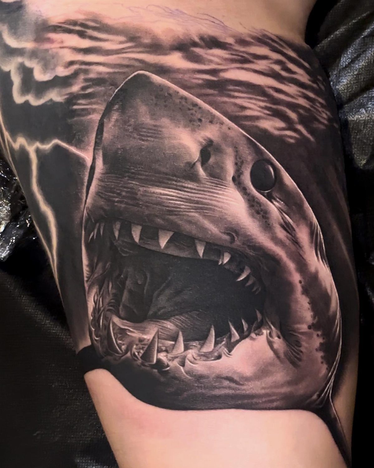 Great white shark tattoo with open jaws and stylized ocean waves on skin