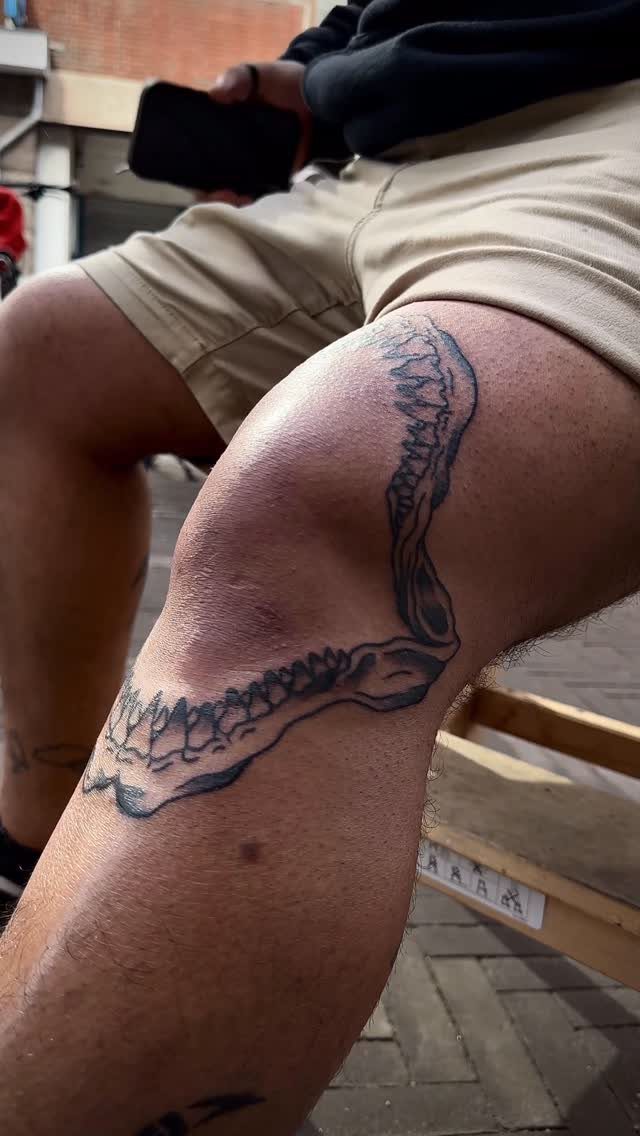 Shark jaw tattoo with sharp teeth wrapping around a person's knee and thigh.