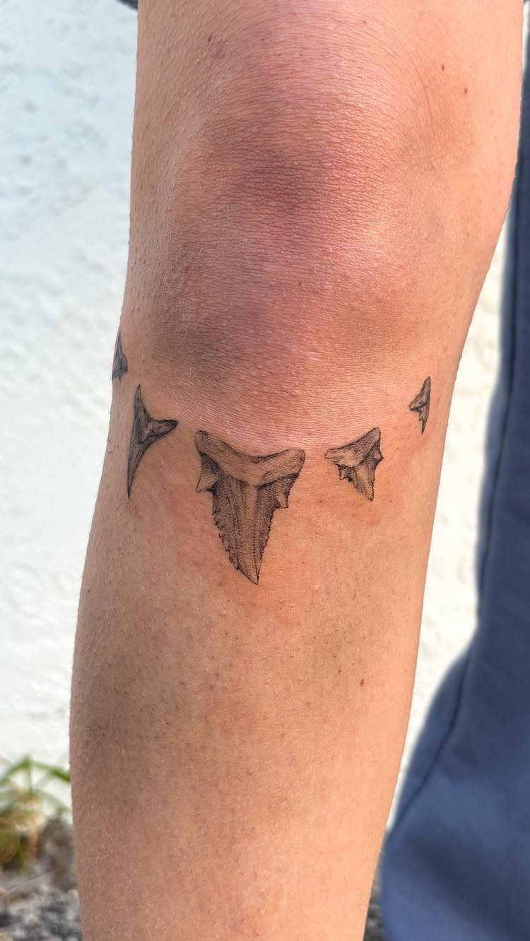 Shark teeth tattoo wrapped around a person's knee in black and grey ink.