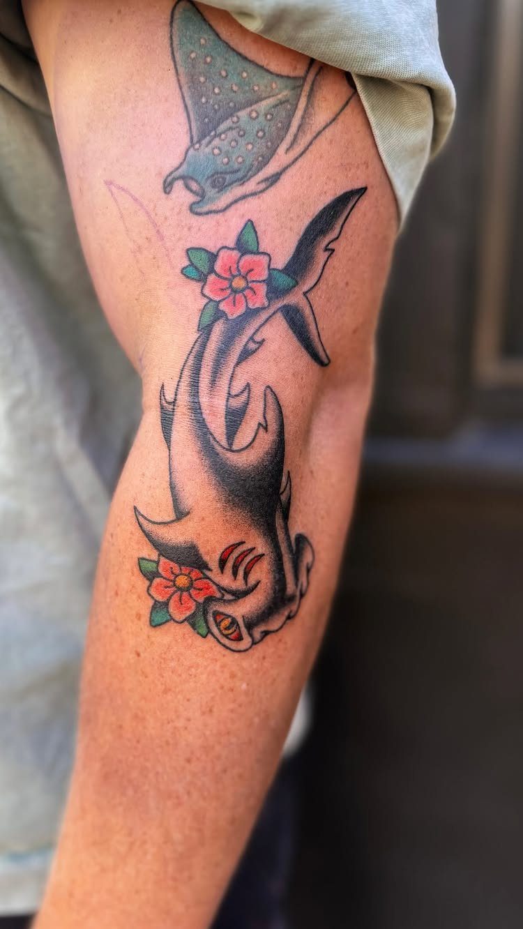 Traditional shark tattoo with red flowers and a stingray on a person's arm.