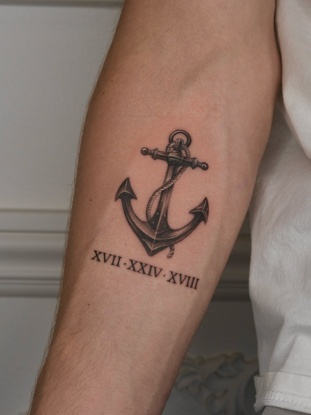 Anchor tattoo with rope and Roman numerals on a person's inner forearm